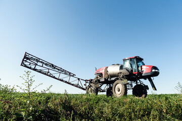 Self-propelled sprayer sprays green corn on the field front view from the side.