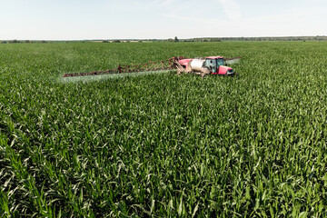 Self-propelled sprayer sprays green corn with pesticides on a photo field from a drone. The tractor sprays the grass with pesticides.