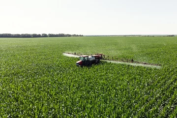 Gordijnen Self-propelled sprayer sprays green corn with pesticides on a photo field from a drone. The tractor sprays the grass with pesticides. © Денис Константинов