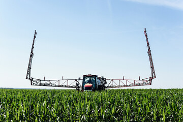 Self-propelled sprayer sprays green corn on the field front view from the side.