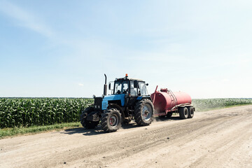 Obraz premium Tractor carries a barrel of water on the field near the corn on a background of sky