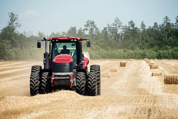 Fototapeta premium Tractor on a field with bales on a background of forest