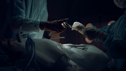 Surgeons team hands suture incision in medical suit dark operating room closeup.