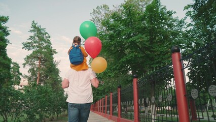Family holiday. Little daughter plays on shoulders of her father, walk in park with balloons....