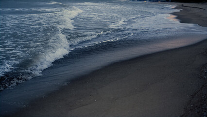 Dark sea waves splashing sandy beach outside. Blue ocean water crashing shore.
