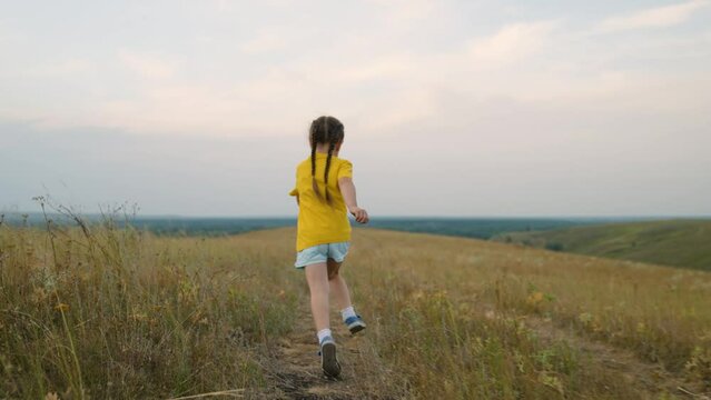 Sports kid. Happy child girl runs along road in yellow grass. Active, cheerful child. Little girl is dreaming in fall in nature. Children's fantasies. Child running across field. Happy family.