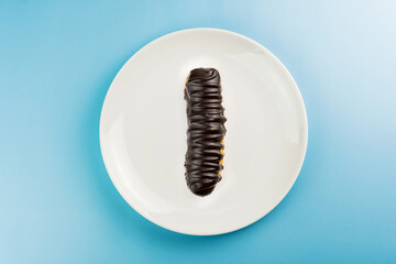 Dessert Bomba de Chocolate. Brazilian traditional éclair in blue plate on the blue table. Top view.
