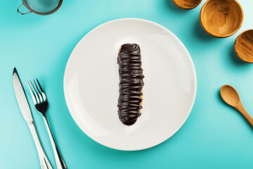 Dessert Bomba de Chocolate. Brazilian traditional éclair in green plate on the yellow table. Top view. Kitchen utensils beside like fork, knife, bamboo containers
