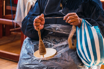 hands of an Andean woman spinning brown alpaca fiber in an ancestral spinning wheel in the Andes...
