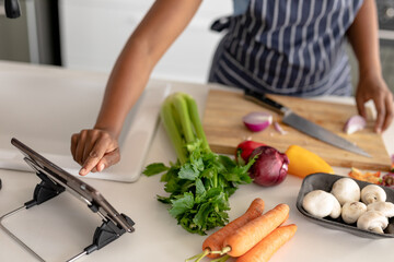 Midsection of african american mid adult woman watching online recipe while preparing food at home