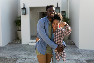 Portrait of cheerful african american young man embracing young girlfriend holding new house key