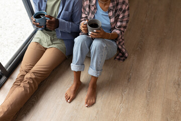 High angle low section of african american young couple with coffee mugs sitting on floor at home