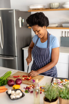 Smiling african american mid adult woman cutting red bell pepper while preparing food at home