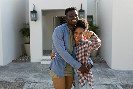 Portrait of cheerful african american young man embracing young girlfriend holding new house key