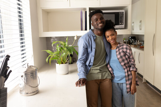 Portrait of smiling african american young man with girlfriend standing by kitchen counter at home