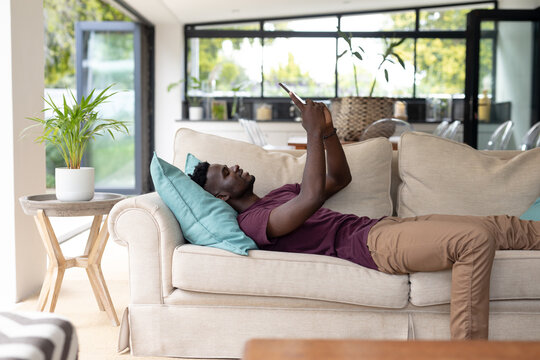 African american young man surfing net over digital tablet while relaxing on sofa in living room