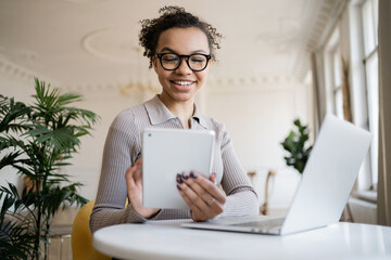 A smart woman with glasses works in a new office, reports the company's earnings online, uses a laptop and tablet.