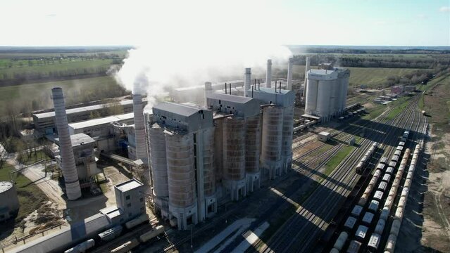 Smoke from pipes of cement plant. Сement Factory with smoke pipe. Chimney smokestack emission. Cement freight cars on railway. Transport bulk materials on railroad. Tank cars near industrial plant.
