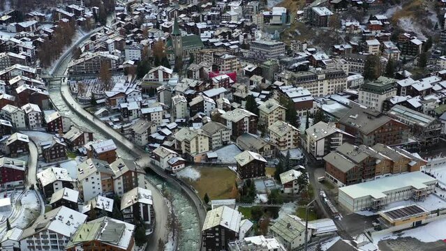 A flight over the small mountain town of Zermatt, high in the Swiss Alps, on a sunny day. Vibrant green grass with remnants of the recent snow, melting away.