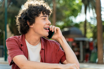 Fototapeta premium Man talking with friend on phone and looking away while sitting at the green park outdoors