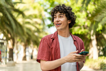 Smiling young man with curly hair reading messages on smartphone
