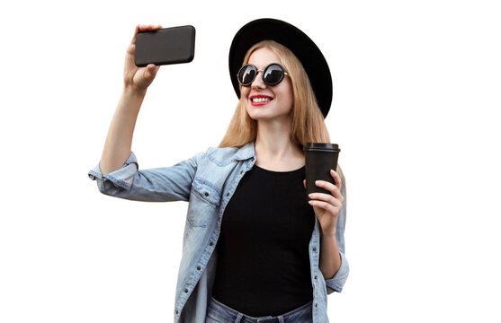 Portrait of happy smiling young woman taking selfie by smartphone wearing black round hat isolated on white background