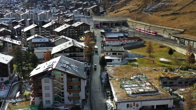 A flight over the small mountain town of Zermatt, high in the Swiss Alps, on a sunny day. Vibrant green grass with remanats of the recent snow, melting away.