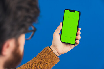 Unrecognizable caucasian guy with a beard and glasses holding a mobile phone with a mockup green...