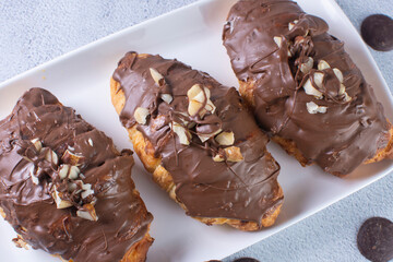 Chocolate croissant with walnut pieces, displayed on gray background