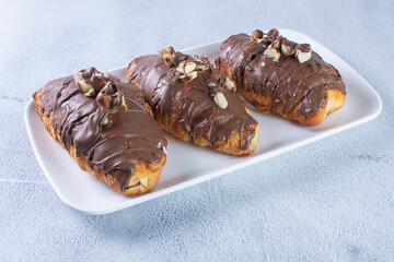 Chocolate croissant with walnut pieces, displayed on gray background