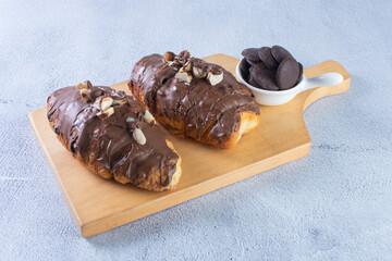 Chocolate croissant with walnut pieces, displayed on gray background