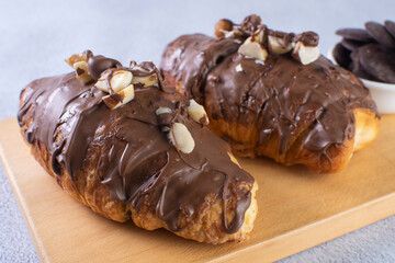 Chocolate croissant with walnut pieces, displayed on gray background