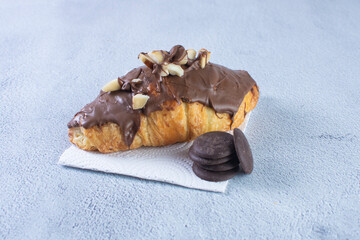 Chocolate croissant with walnut pieces, displayed on gray background