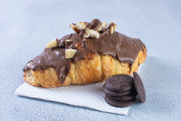 Chocolate croissant with walnut pieces, displayed on gray background