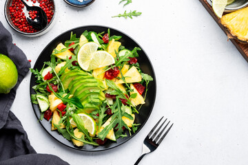 Summer vegan salad with juicy pineapple, fresh arugula, avocado and dried cranberry on white stone kitchen table, top view. Healthy eating, clean diet food, weight loss concept