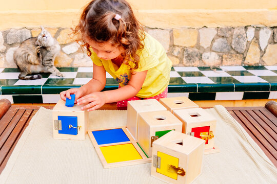 A girl learns using her hands to play with wooden boxes with locks with montessori pedagogy.