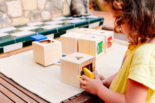 A girl manipulates sensory montessori material, wooden boxes to fit cubes.