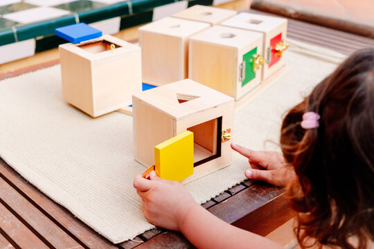 A girl learns using her hands to play with wooden boxes with locks with montessori pedagogy.