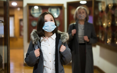 Fototapeta na wymiar Portrait of inquisitive preteen girl wearing protective face mask visiting exposition in historical museum during coronavirus pandemic