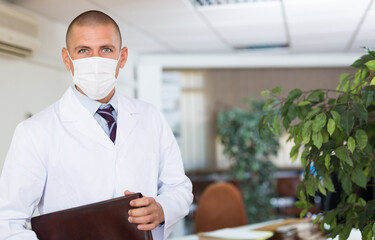 Fototapeta na wymiar Portrait of male doctor in protective mask in the office of a modern clinic