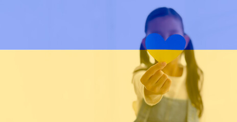 Ukraine flag with unidentified little girl is holding the paper heart to pray for Ukraine, concept...