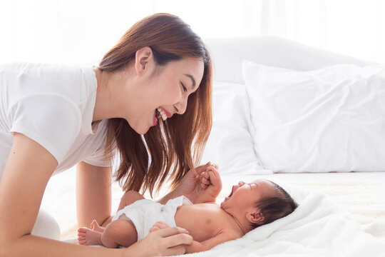 Beautiful Young Mother And Toddler Lying In Bedroom Talking Or Singing Together. Singlemom Playing With Cute Newborn Baby And Spend Time Together On Bed, Mom Looking Infant With Love And Tender.