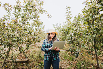 Young latin farmer woman using a laptop to control the production of her farmland.