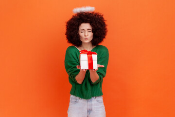 Positive funny angelic woman with Afro hairstyle wearing green casual style sweater giving wrapped...