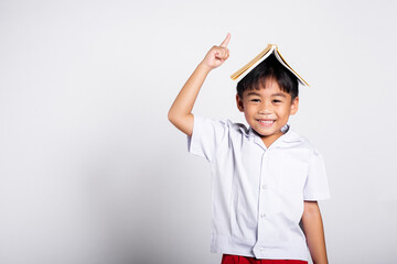 Asian adorable toddler smiling happy wearing student thai uniform red pants stand holding book over...