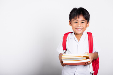 Asian adorable toddler smiling happy wearing student thai uniform red pants stand books for study...