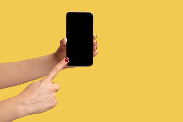 Fototapeta na wymiar Profile side view closeup of woman hand holding and showing smart phone and pointing at empty display. Indoor studio shot isolated on yellow background.