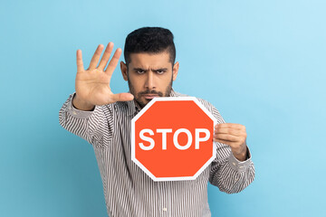 Businessman holding octagonal Stop symbol, showing red traffic sign and ban gesture with palm,...