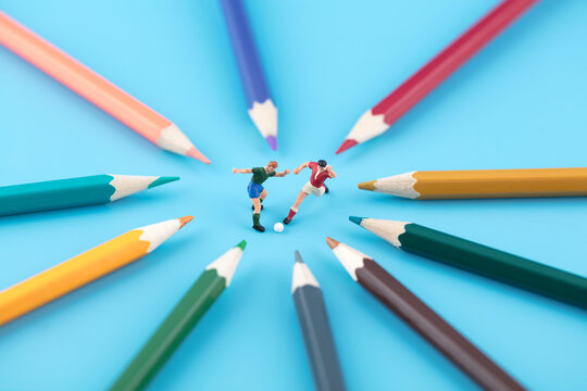 Miniature world player kicks ball surrounded by colored pencils