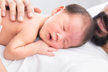 Close up of Asian newborn baby sleeping on his father's chest. Dad and son spend time together at home, young dad with cute little infant in his arms. Father and toddler in bed in the morning.